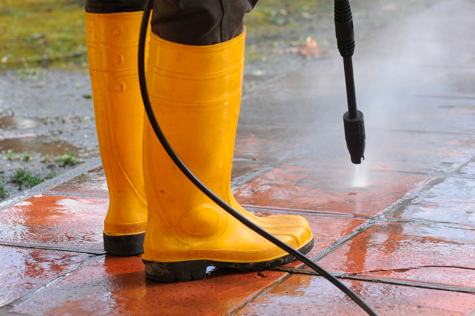 Person with yellow rubber boots using a pressure washer